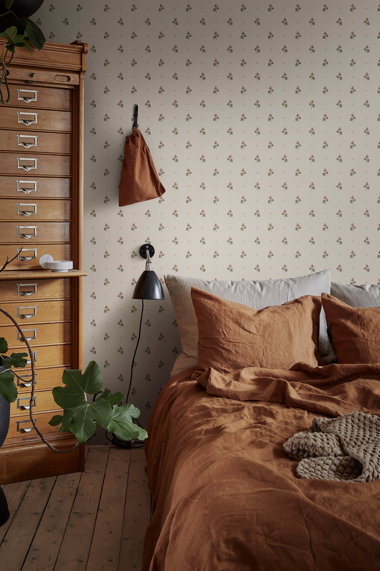 Mimi wallpaper by Sandberg in a bedroom, delicate violet-sprig pattern behind a rust linen bed and antique card-file cabinet