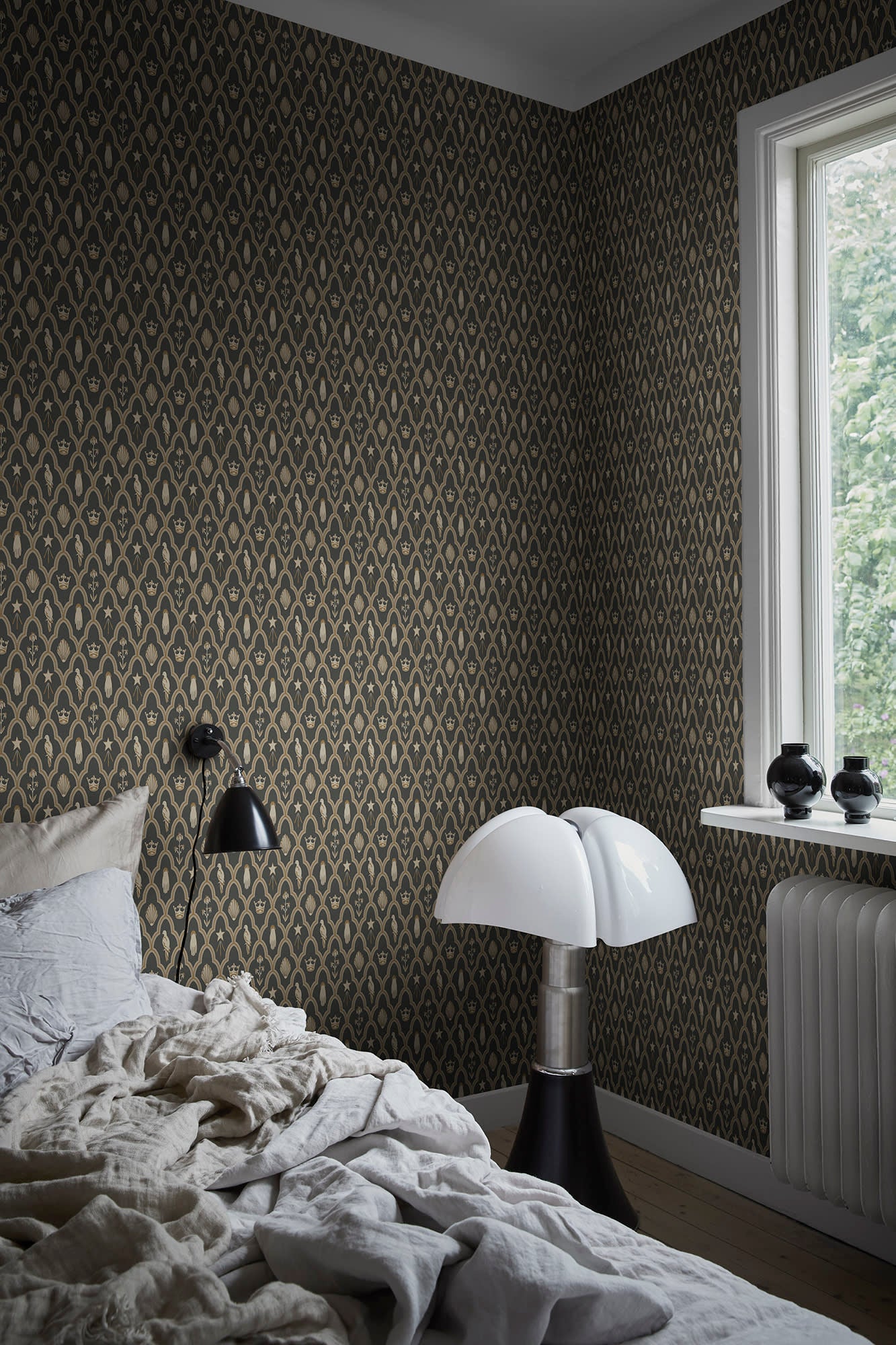 Turtledove Barn wallpaper by Sandberg in charcoal-gold styled in a bedroom with rumpled linen, a sculptural lamp and bright window