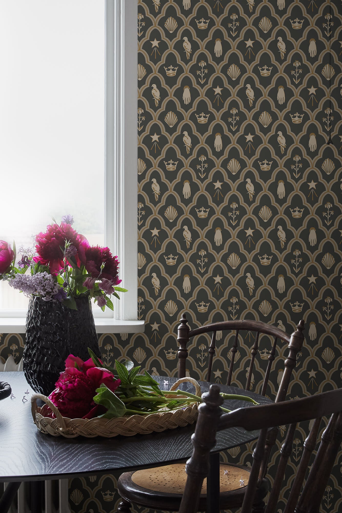 Turtledove Barn wallpaper by Sandberg in charcoal and gold styled in a dining room with a window, dark chair and pink peonies