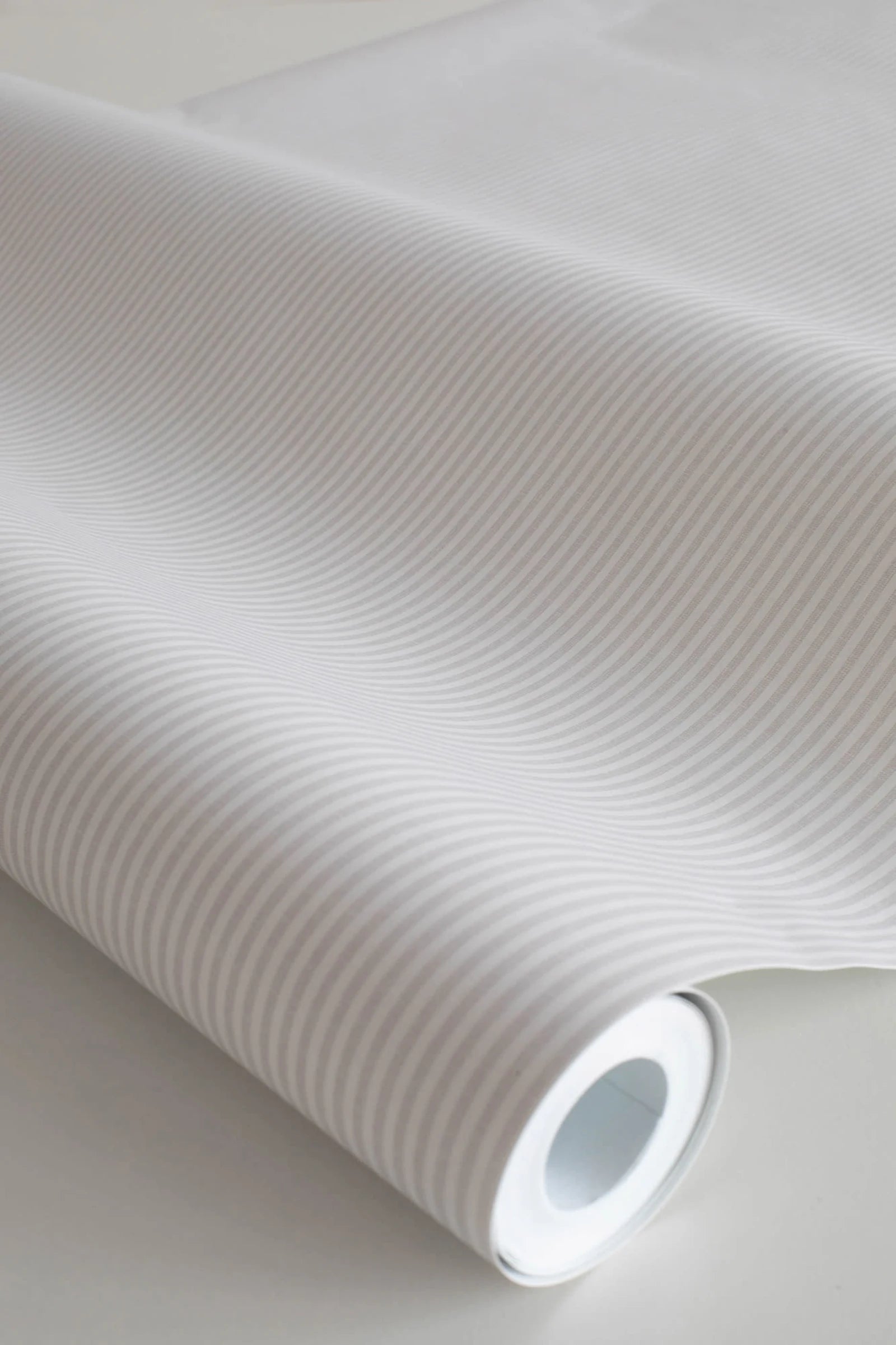 Rand Stripe wallpaper by Sandberg in greige, close-up of a wallpaper roll showing a fine ticking pinstripe