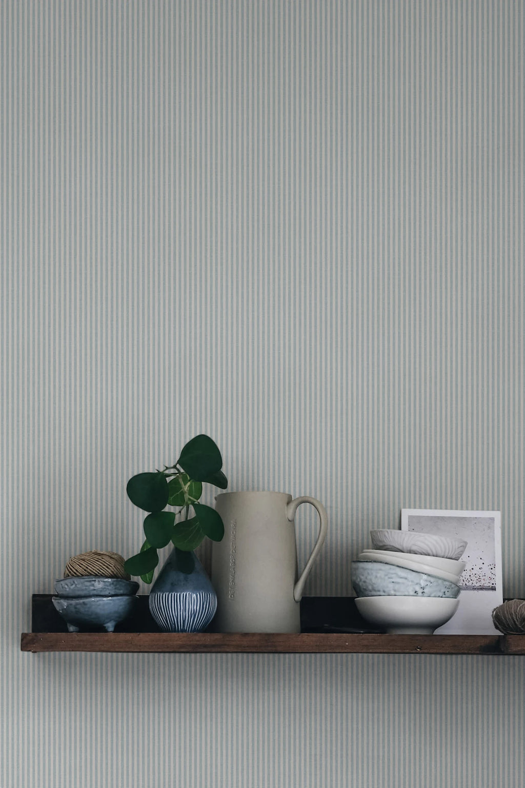 Rand Stripe wallpaper by Sandberg in soft sage-grey, styled above a timber shelf with jug, plant and ceramic bowls