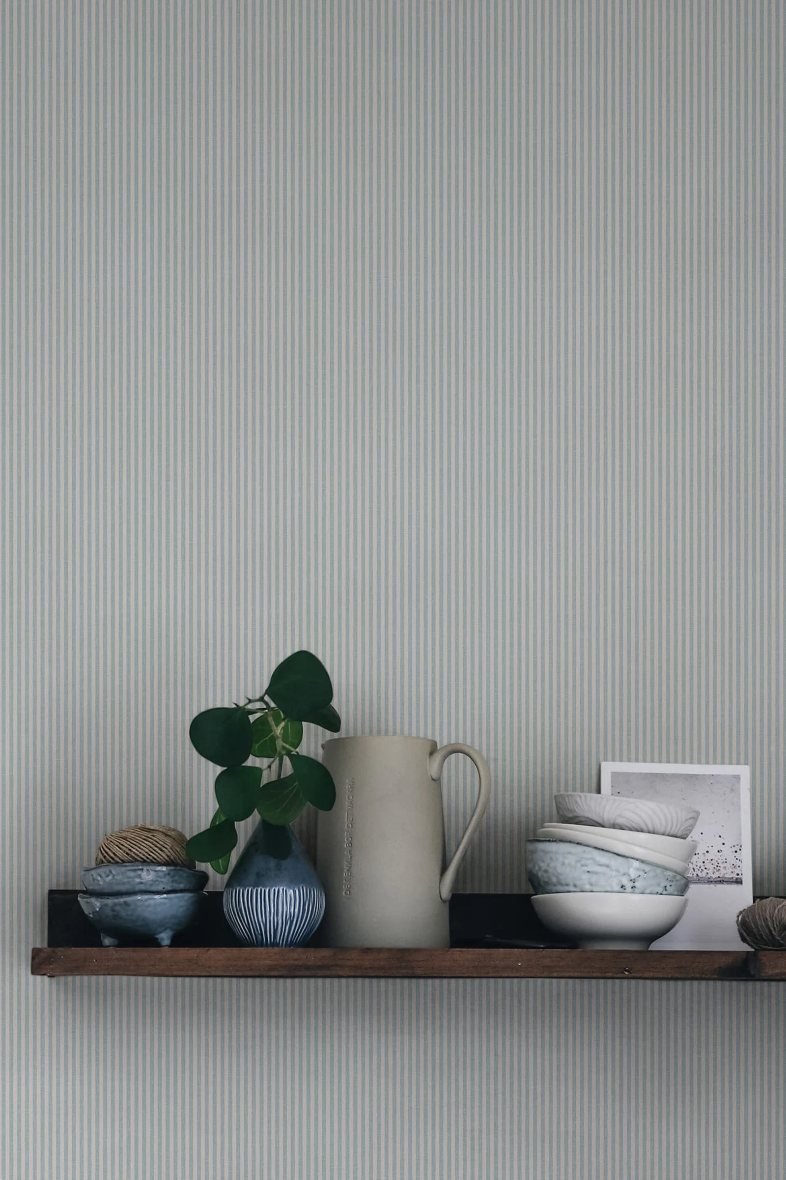 Rand Stripe wallpaper by Sandberg in soft sage-grey, styled above a timber shelf with jug, plant and ceramic bowls