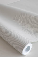 Rand Stripe wallpaper by Sandberg in pale oatmeal, close-up of a wallpaper roll showing a fine ticking pinstripe