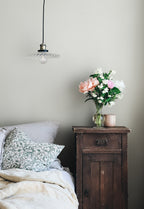 Valv wallpaper by Sandberg in cream in a bedroom beside a rustic timber nightstand with flowers and a glass pendant