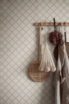 Trellis wallpaper by Sandberg in sage green behind a peg rail holding a linen apron, rattan tray and dried flowers