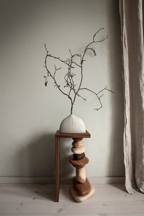 Bladverk wallpaper by Sandberg in muted sage with a dried branch arrangement in a white vase atop a stacked-stone stool