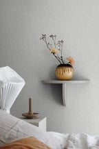 Bladverk wallpaper by Sandberg in grey-green behind a bed, with a floating shelf holding a glazed vase of dried flowers