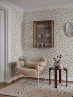 Bokskog wallpaper by Sandberg in a living corner, green birch leaf pattern behind a glass cabinet and shearling chair