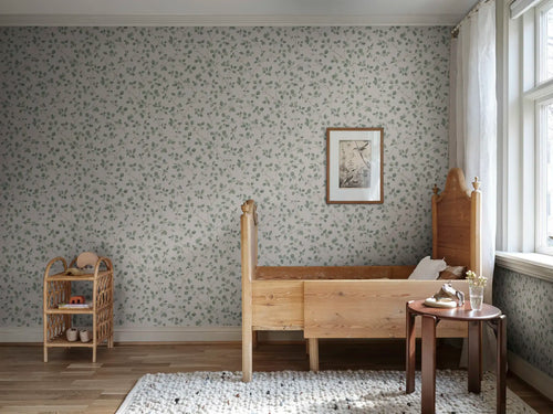 Bokskog wallpaper by Sandberg in a nursery, soft green leaf trails behind a timber cot and rattan shelf