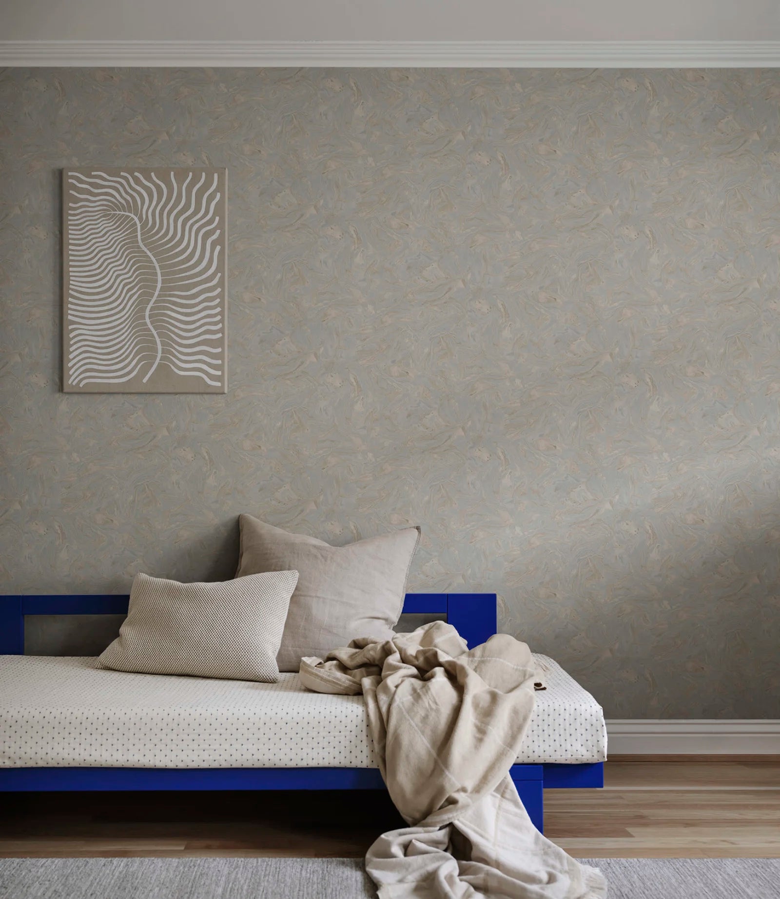 Marion marbled wallpaper by Sandberg in blue-grey behind a cobalt daybed, viewed across a styled bedroom