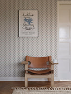 Betty wallpaper by Sandberg styled in a hallway, coral and blue tulip-sprig pattern behind a tan leather chair and framed art print