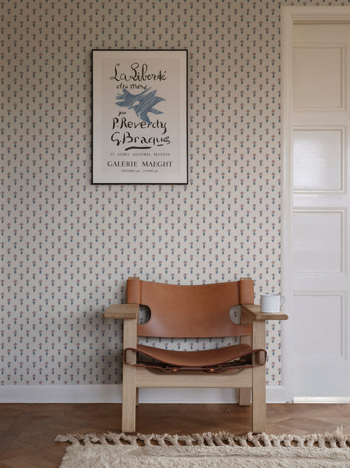 Betty wallpaper by Sandberg styled in a hallway, coral and blue tulip-sprig pattern behind a tan leather chair and framed art print