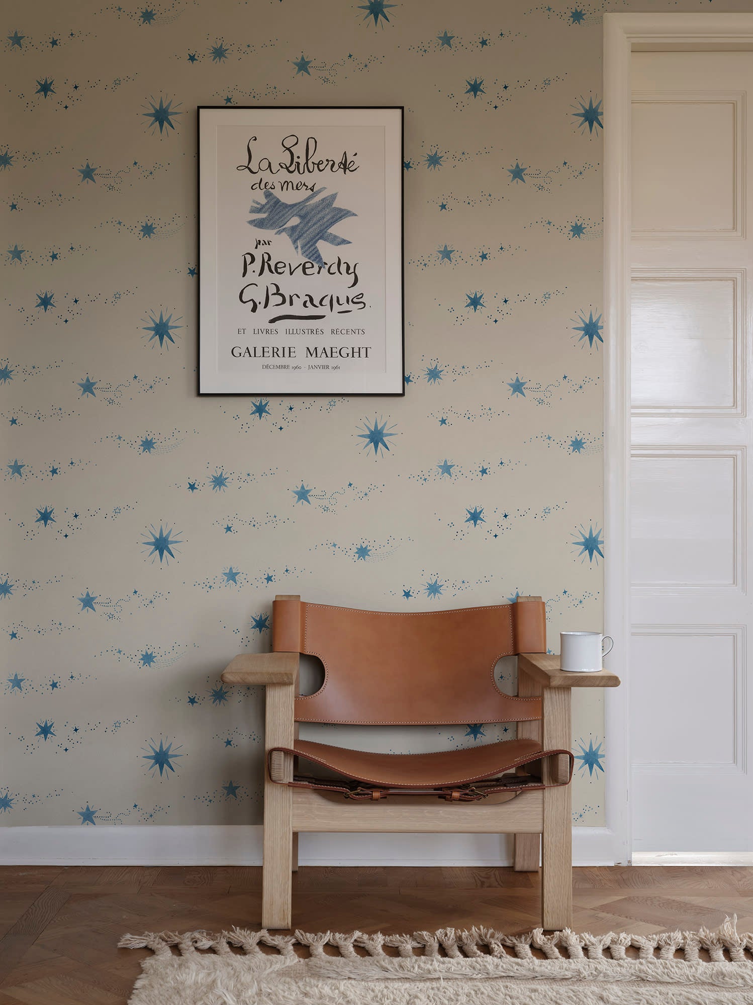 Gillis blue star mural by Sandberg behind a tan leather chair and framed vintage poster.