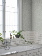 Soft grey-green Karolina leaf wallpaper by Sandberg above white subway tiles by a bathtub and window