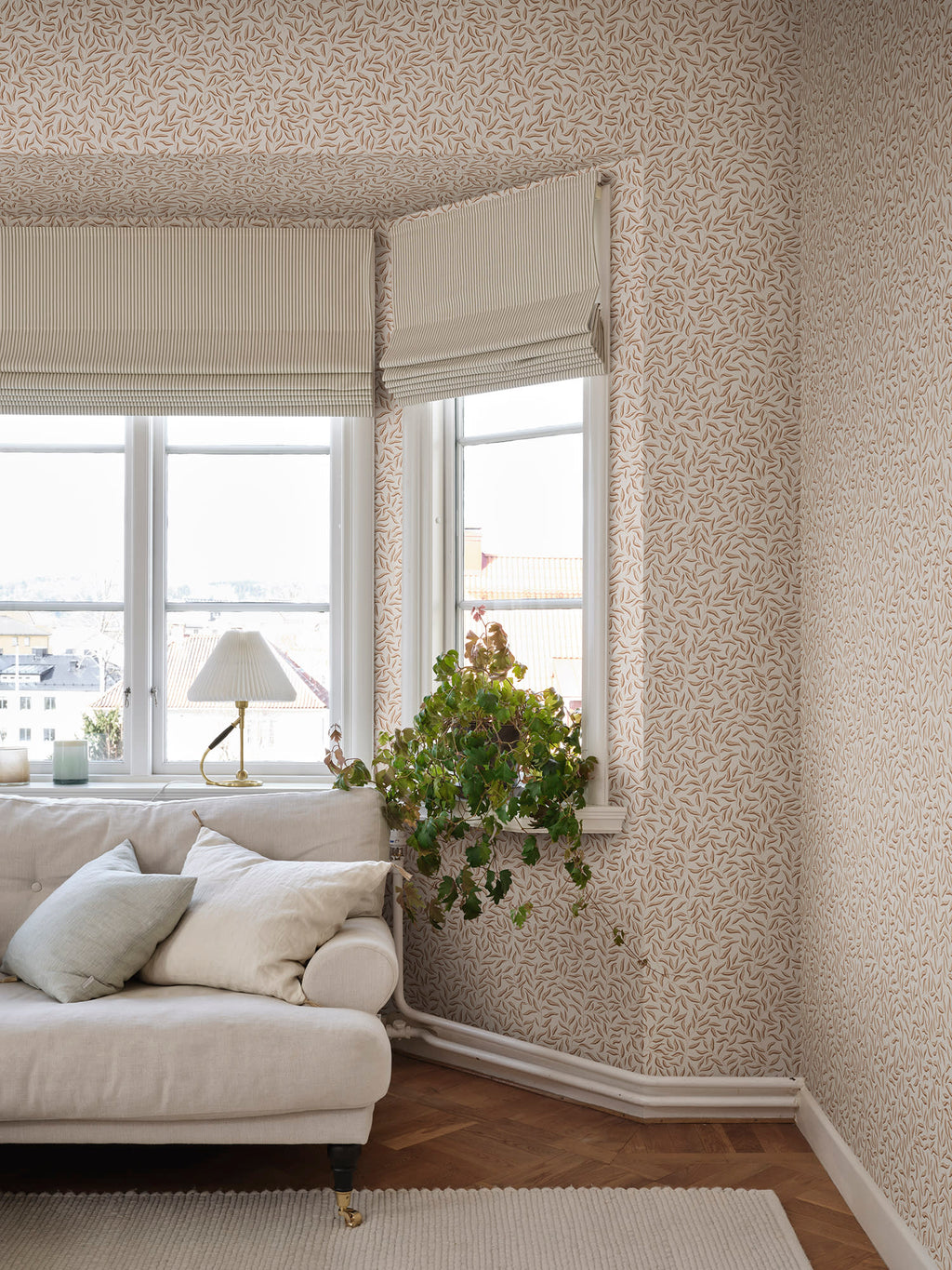 Beige Karolina trailing-leaf wallpaper by Sandberg in a living room with neutral sofa and roman blinds