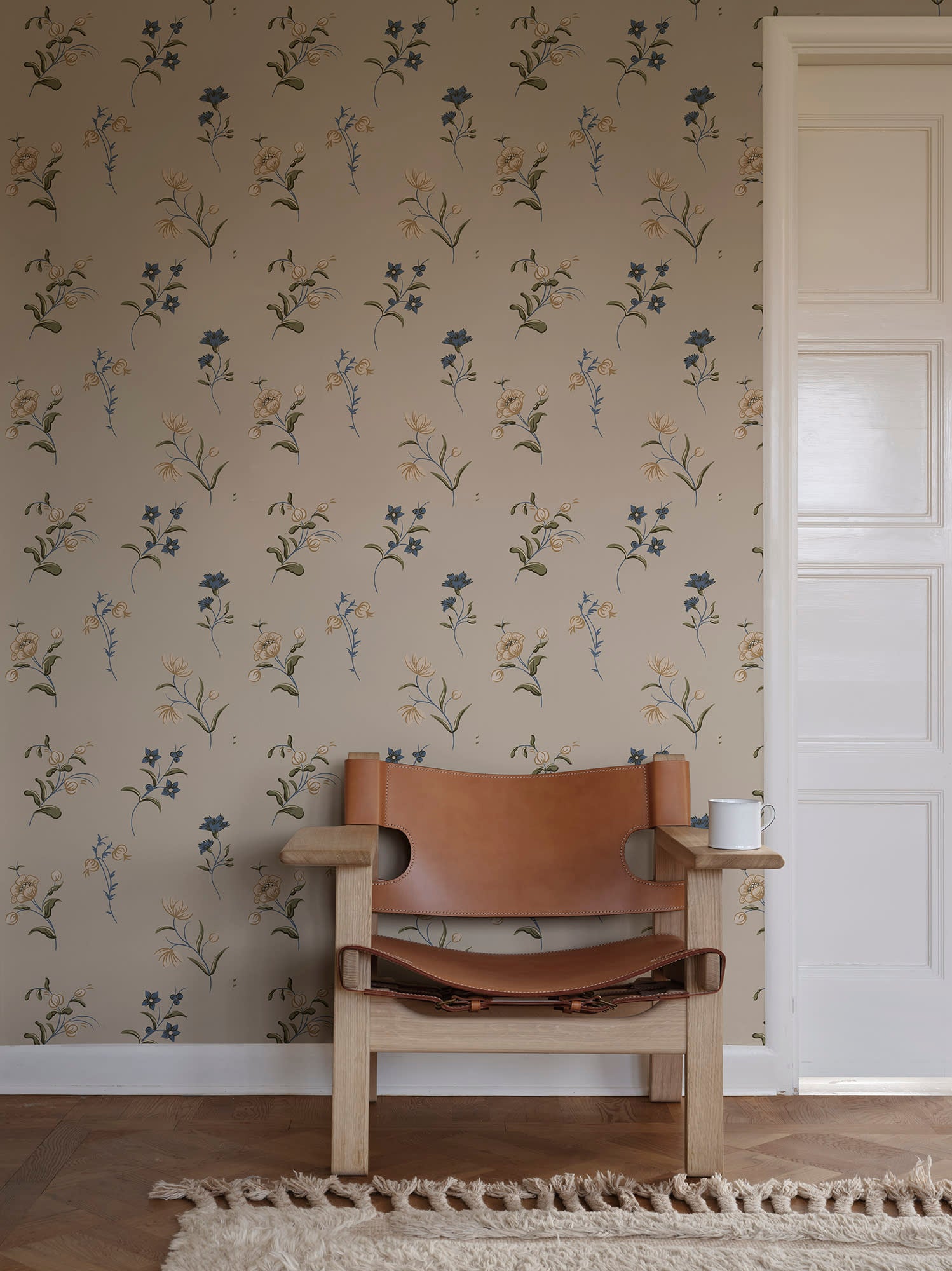 Hanna wallpaper by Sandberg in beige behind a tan leather sling chair on a fringed rug