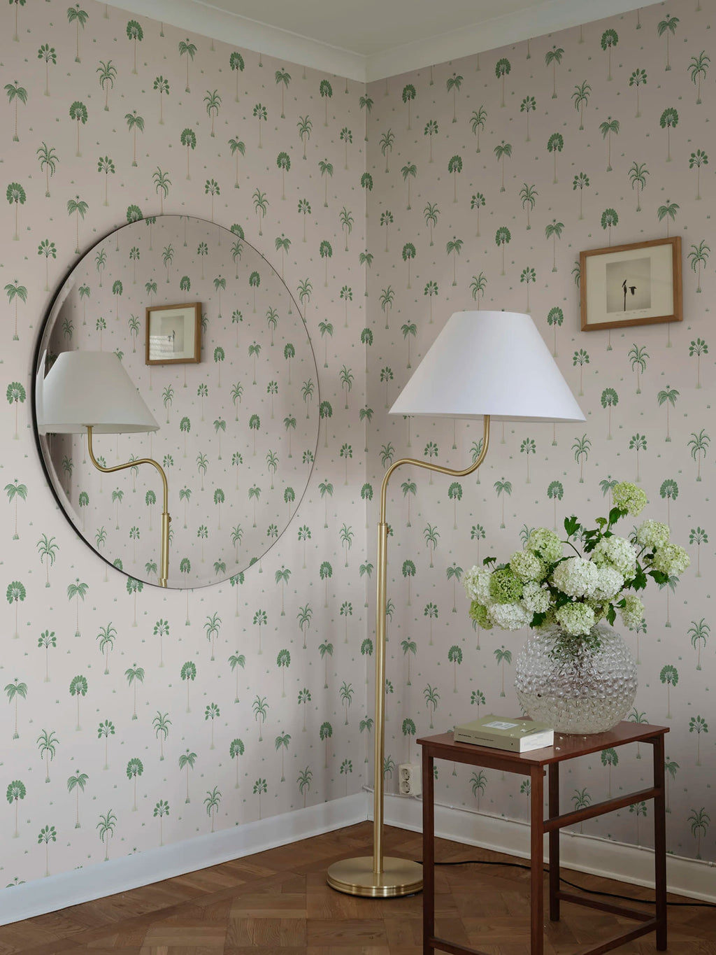 Milo Palms wallpaper by Sandberg in green on blush, styled in a corner with a round mirror, brass floor lamp and hydrangeas