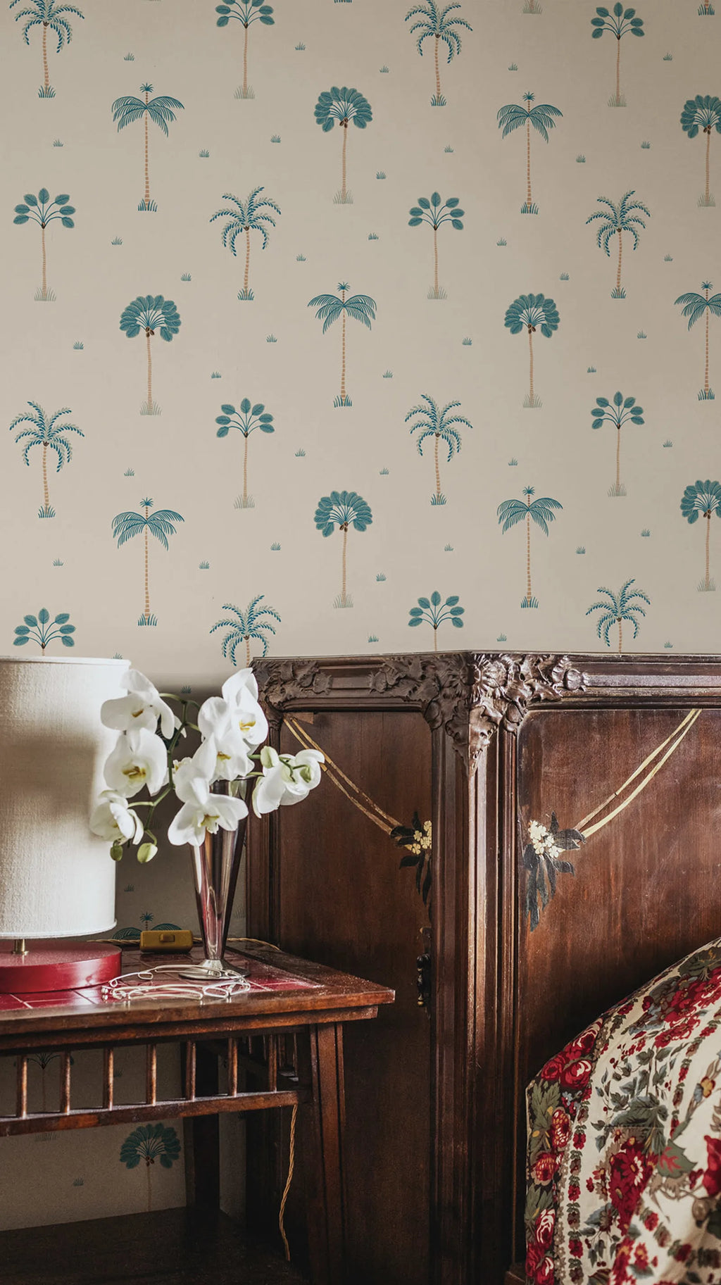 Milo Palms wallpaper by Sandberg in teal on cream, styled in a bedroom above a dark wood dresser with white orchids