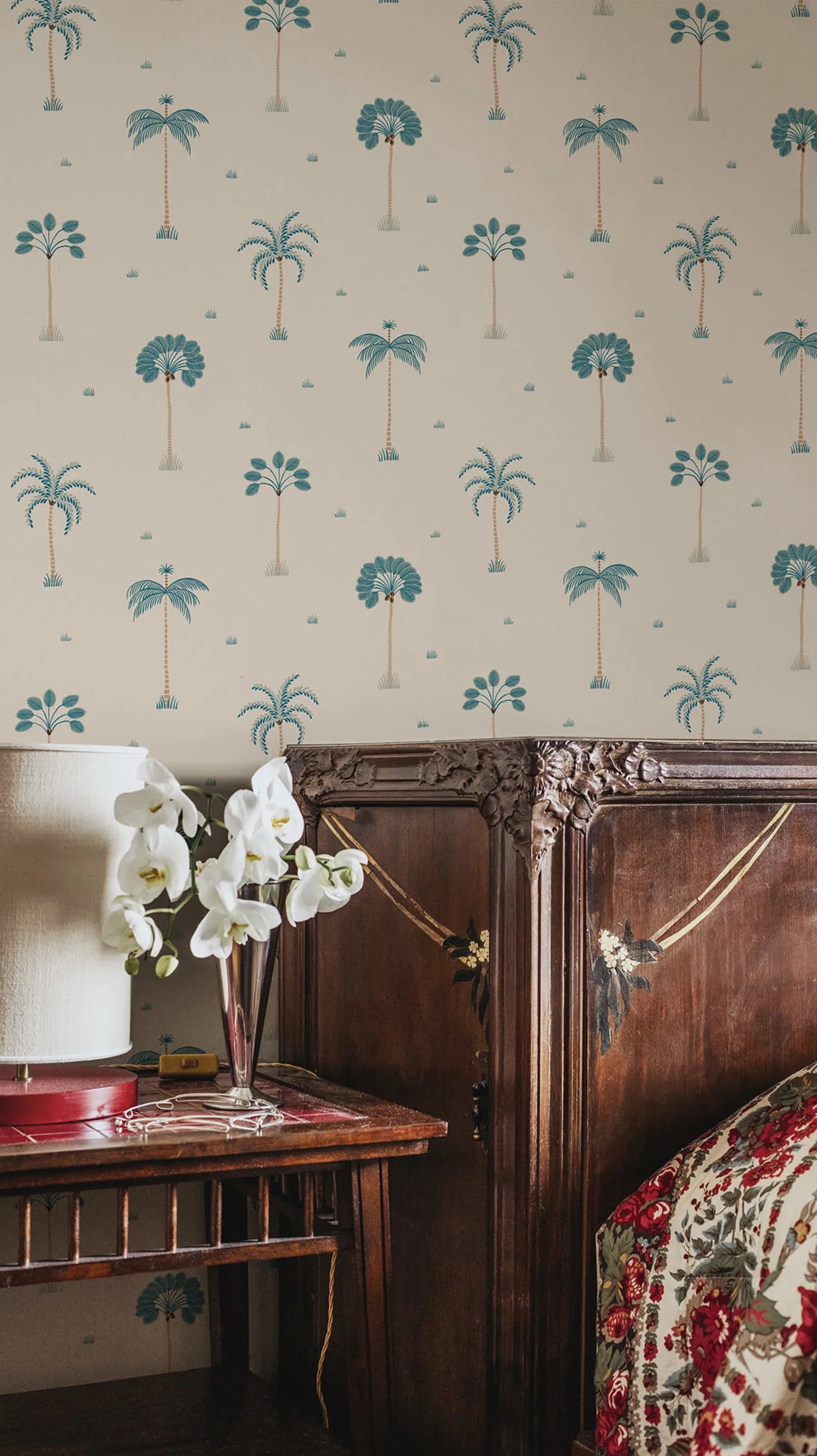 Milo Palms wallpaper by Sandberg in teal on cream, styled in a bedroom above a dark wood dresser with white orchids