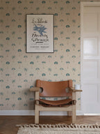 Milo Palms wallpaper by Sandberg in teal on cream, styled behind a tan leather safari chair and framed art print