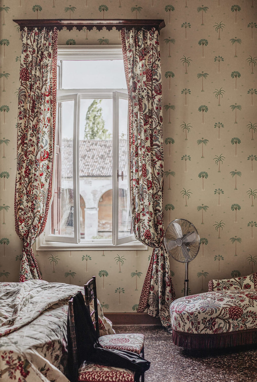 Milo Palms wallpaper by Sandberg in green on sand, styled in a heritage bedroom with red floral curtains and an open window