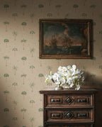 Milo Palms wallpaper by Sandberg in green on sand, styled behind an antique chest topped with a framed seascape and white orchids