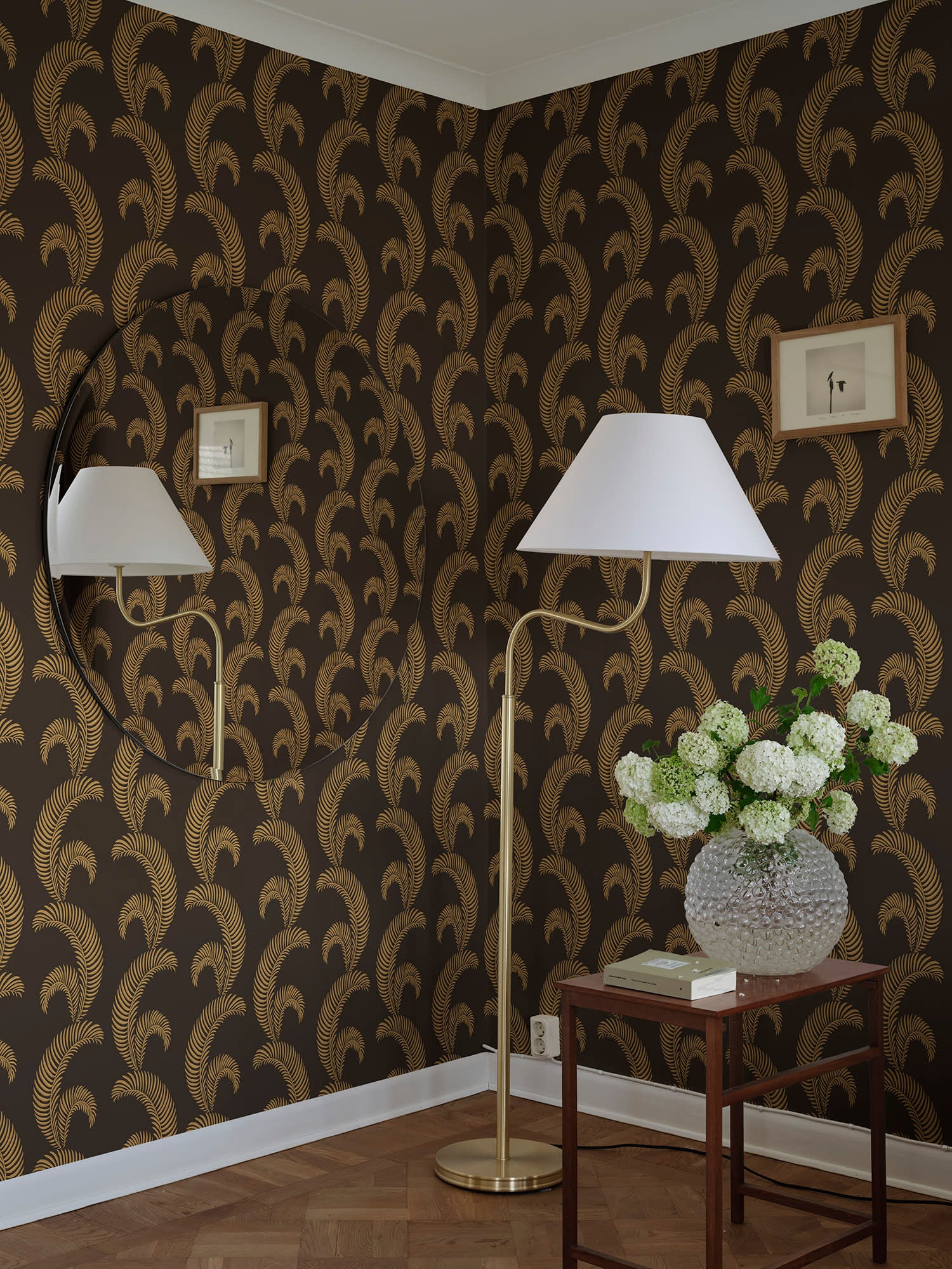 Jasmine wallpaper by Sandberg in gold on brown behind a floor lamp and side table with white hydrangeas