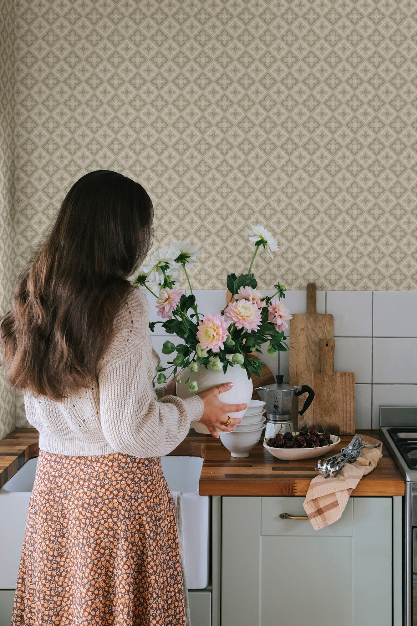 Edvin wallpaper by Sandberg in sage green styled in a kitchen behind a woman arranging dahlias