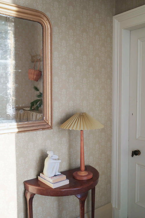 Alva wallpaper by Sandberg in beige behind a demilune table with books and a sculpture in an entryway