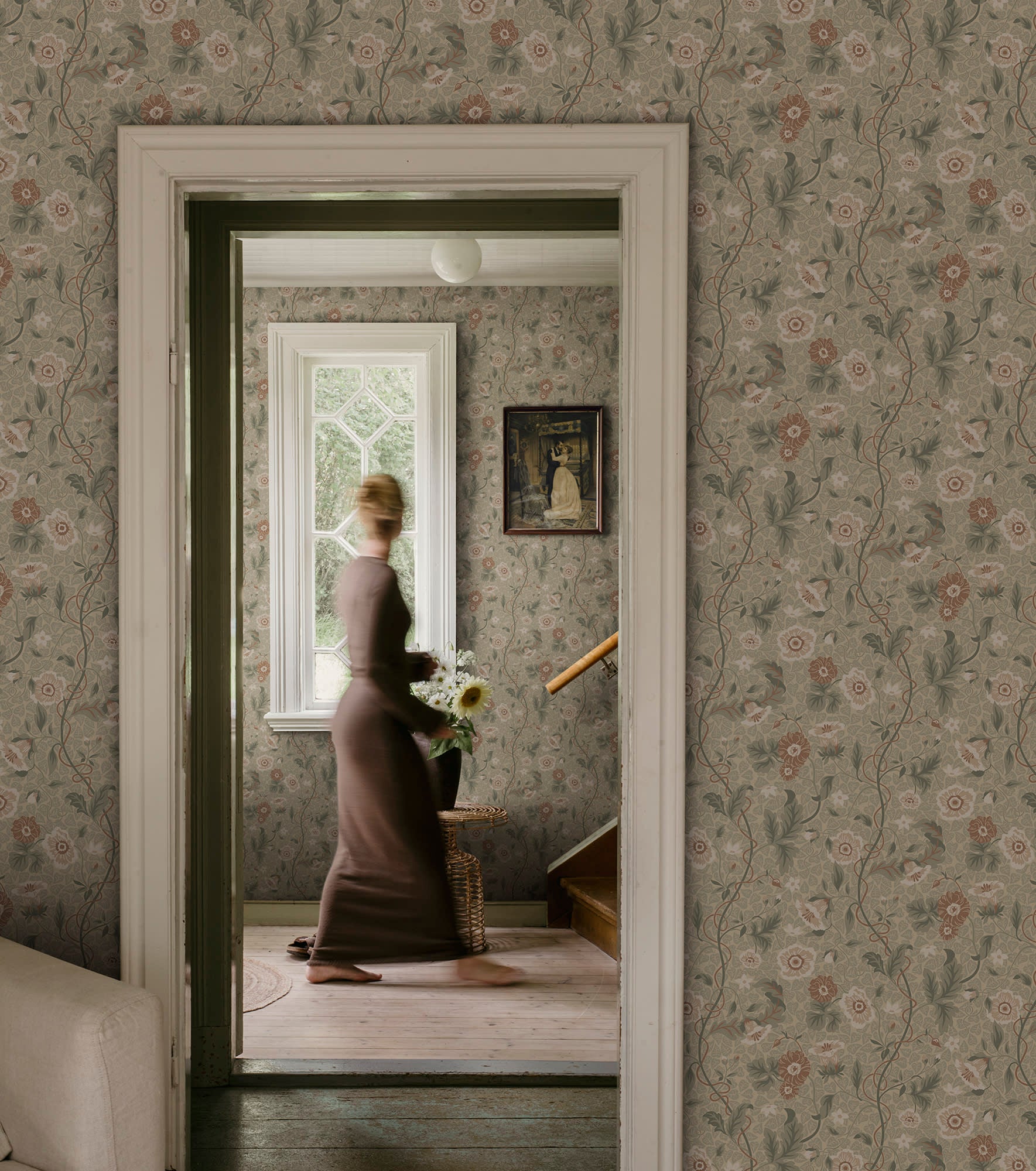 Ulla wallpaper by Sandberg in sage tones styled across a period hallway with a woman walking past a window