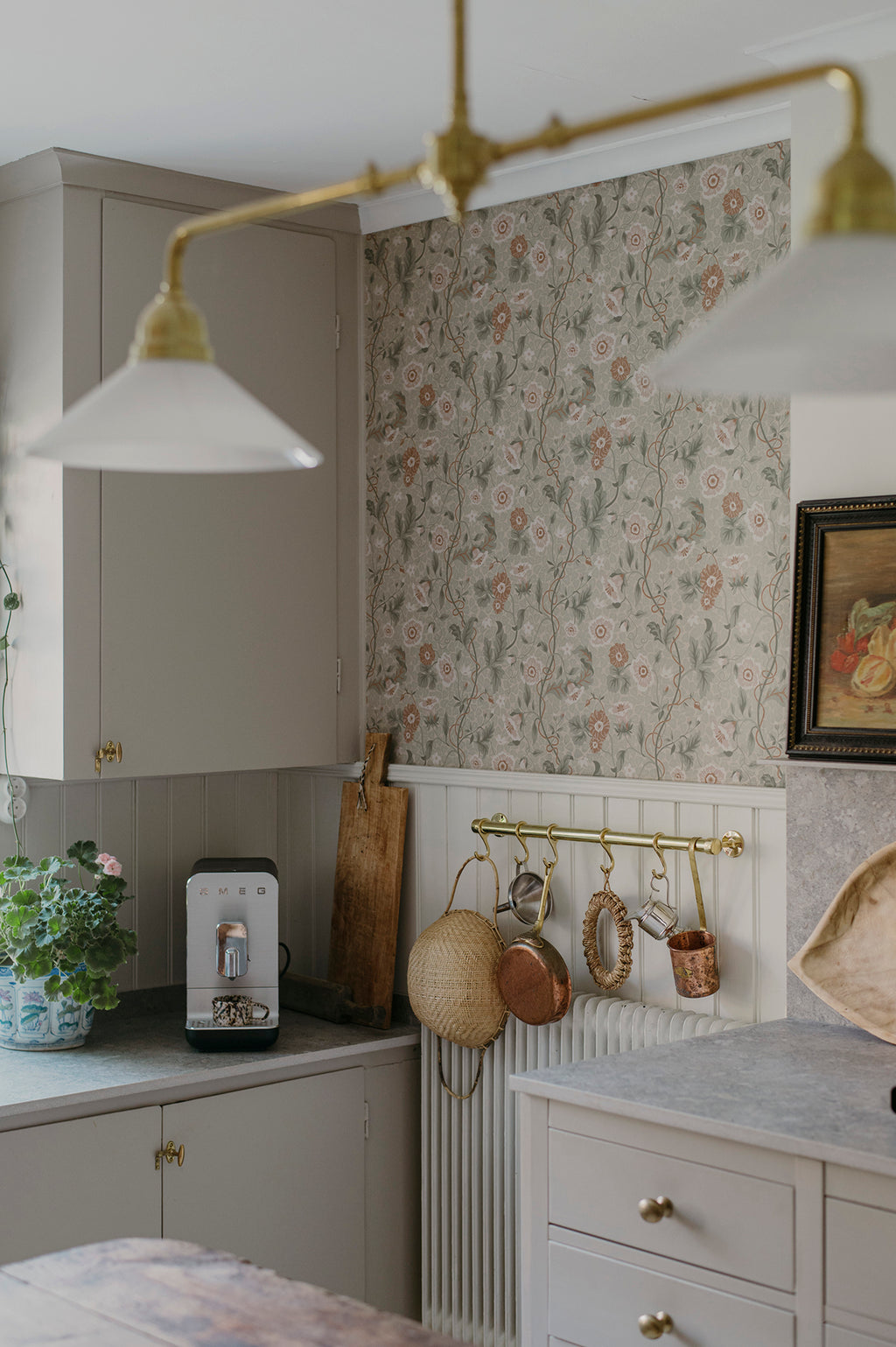 Ulla wallpaper by Sandberg in sage tones on a kitchen wall with brass lighting, panelling and hanging copper pans
