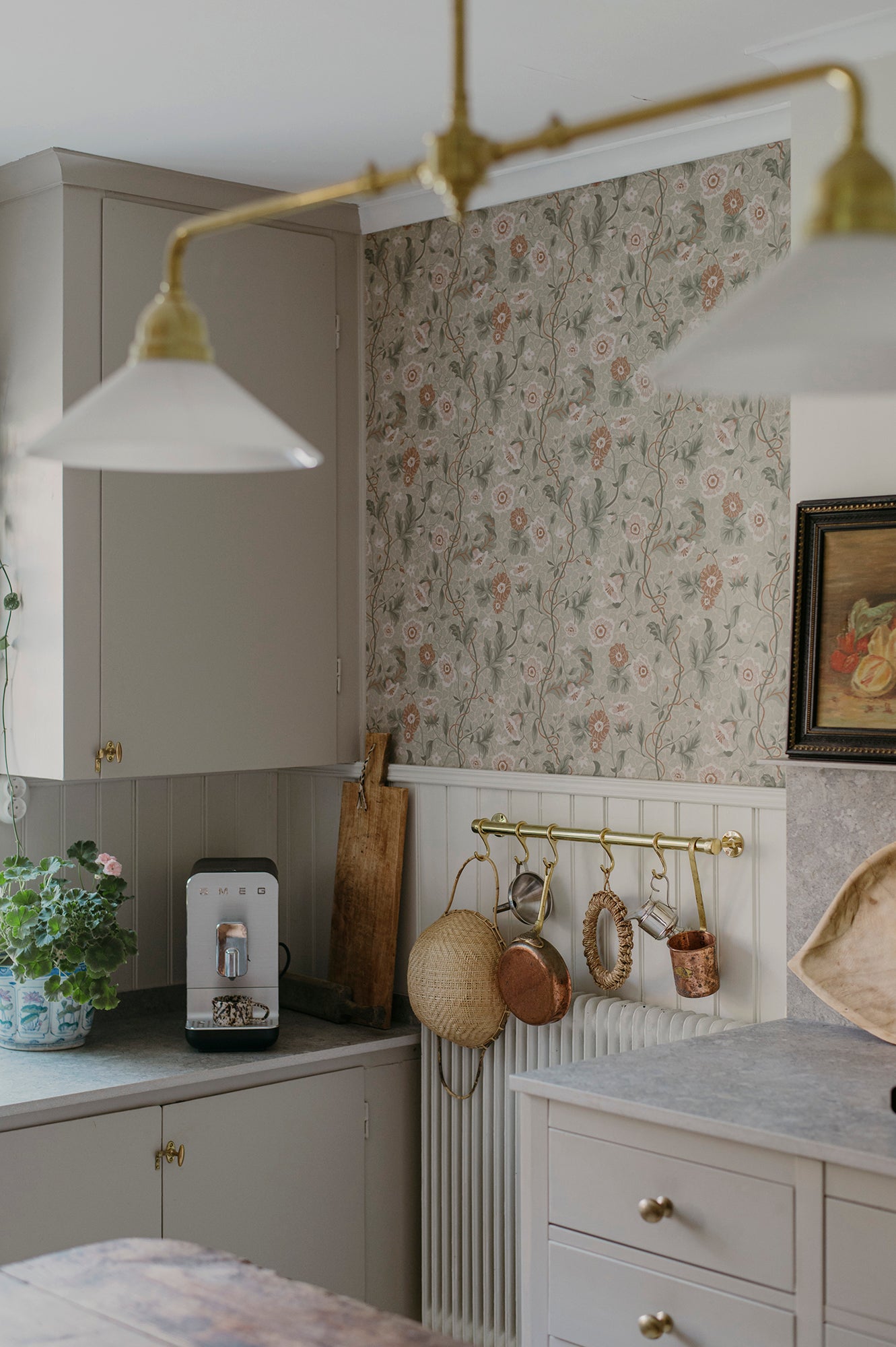 Ulla wallpaper by Sandberg in sage tones on a kitchen wall with brass lighting, panelling and hanging copper pans