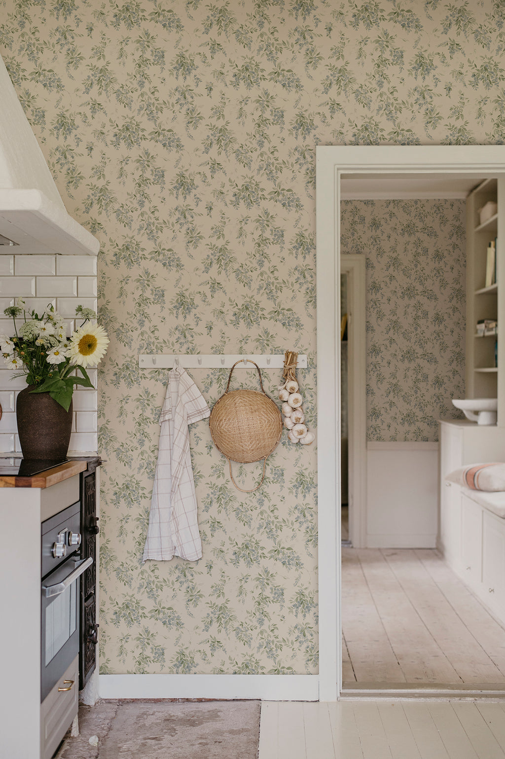 Lovisa wallpaper by Sandberg in green in a kitchen with a peg rail, straw bag and garlic by a doorway