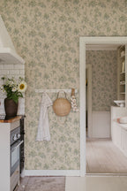 Lovisa wallpaper by Sandberg in green in a kitchen with a peg rail, straw bag and garlic by a doorway