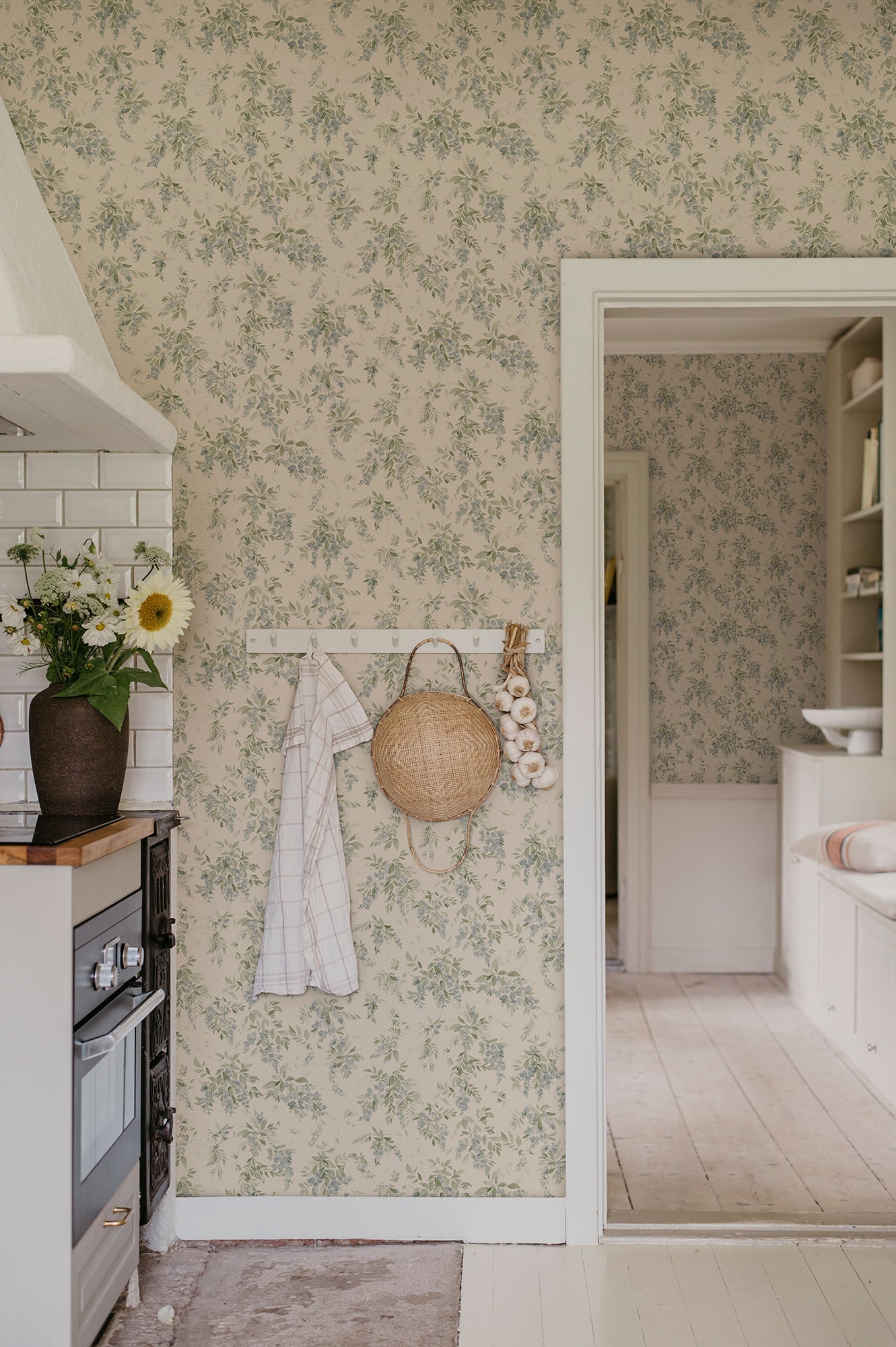 Lovisa wallpaper by Sandberg in green in a kitchen with a peg rail, straw bag and garlic by a doorway