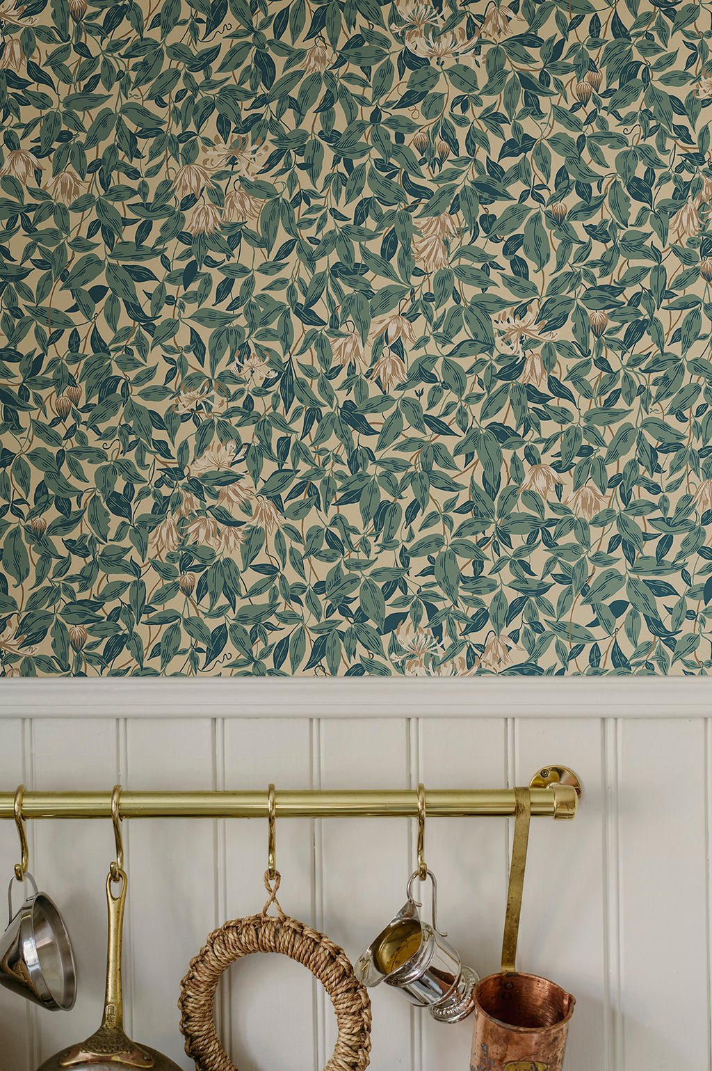Linnea wallpaper by Sandberg, teal honeysuckle close-up above white panelling with a brass rail of copper pans