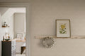 Emil wallpaper by Sandberg in pale sand in a hallway with picture shelf, framed botanical and dried wreath