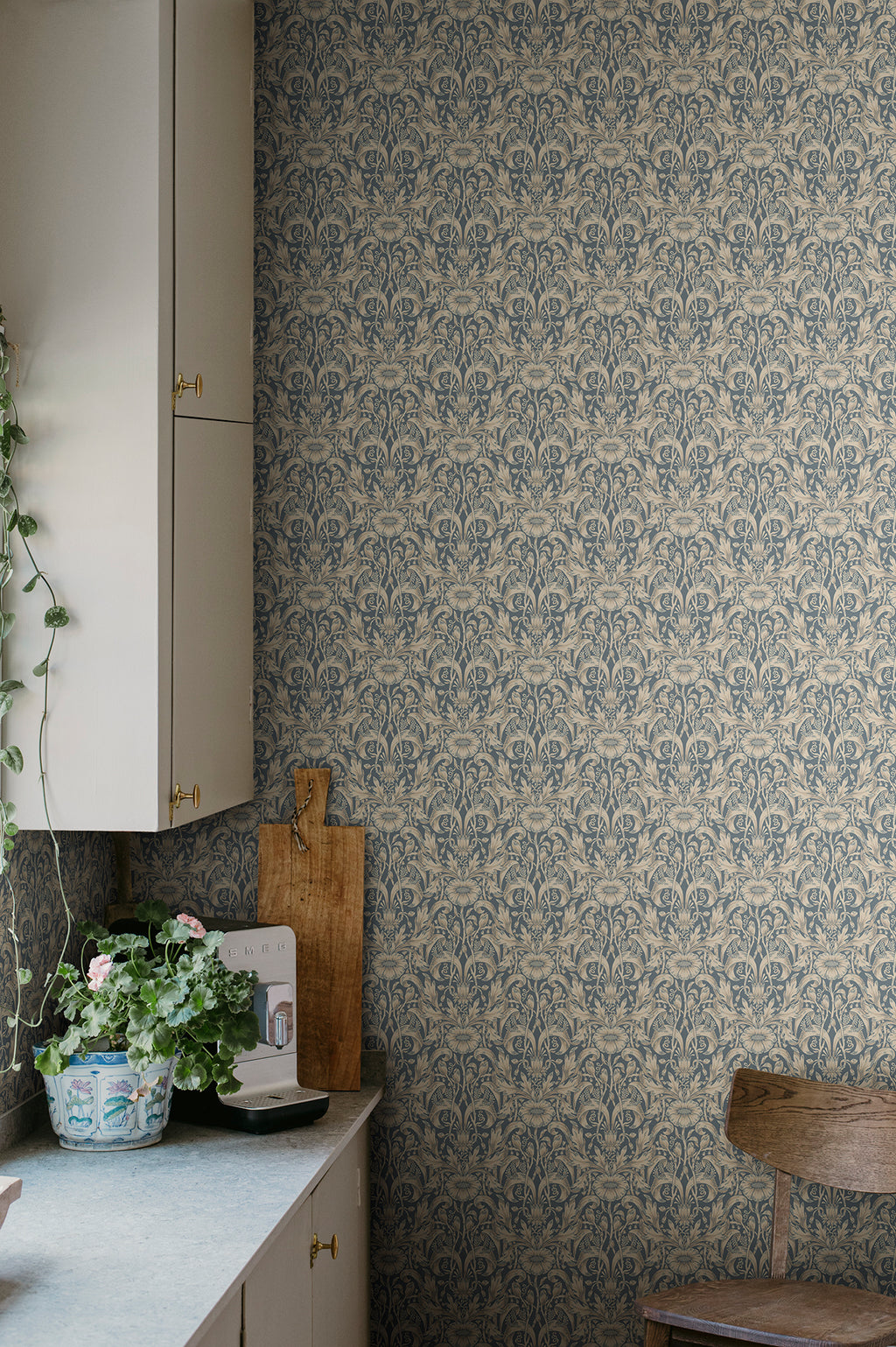 Emil wallpaper by Sandberg in slate blue in a kitchen corner with cream cabinetry and a potted geranium
