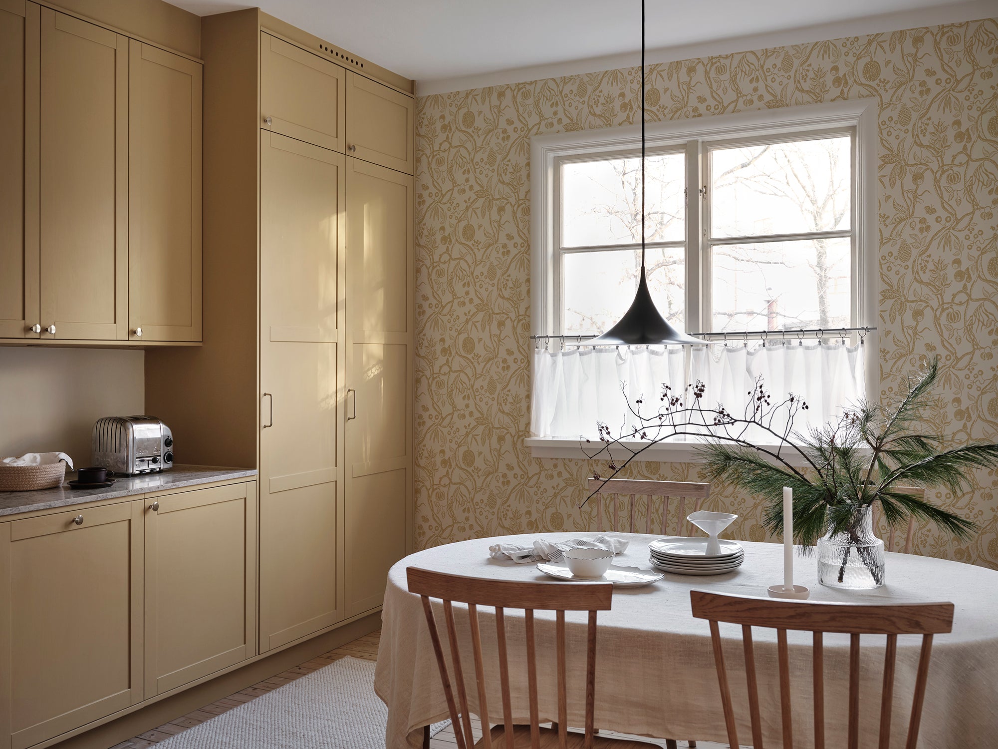 Tree of Life wallpaper by Sandberg in ochre-gold, styled in a kitchen-diner beside a window with timber table and chairs