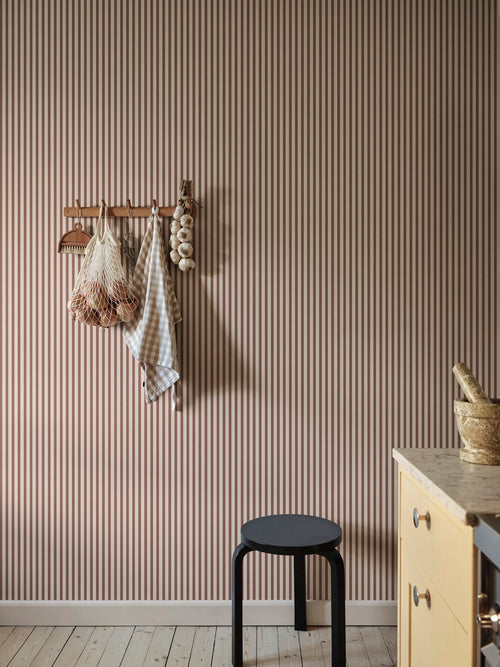 Estelle wallpaper by Sandberg in a rust-red stripe, styled in a kitchen with hanging garlic, gingham cloth and yellow