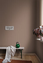 Estelle wallpaper by Sandberg in a brown stripe, styled in a mudroom above a timber bench with a kettlebell and trailing plant