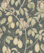 Elliot wallpaper by Sandberg, flat swatch of ring-tailed lemurs among leafy branches and mangoes on a slate grey-green ground