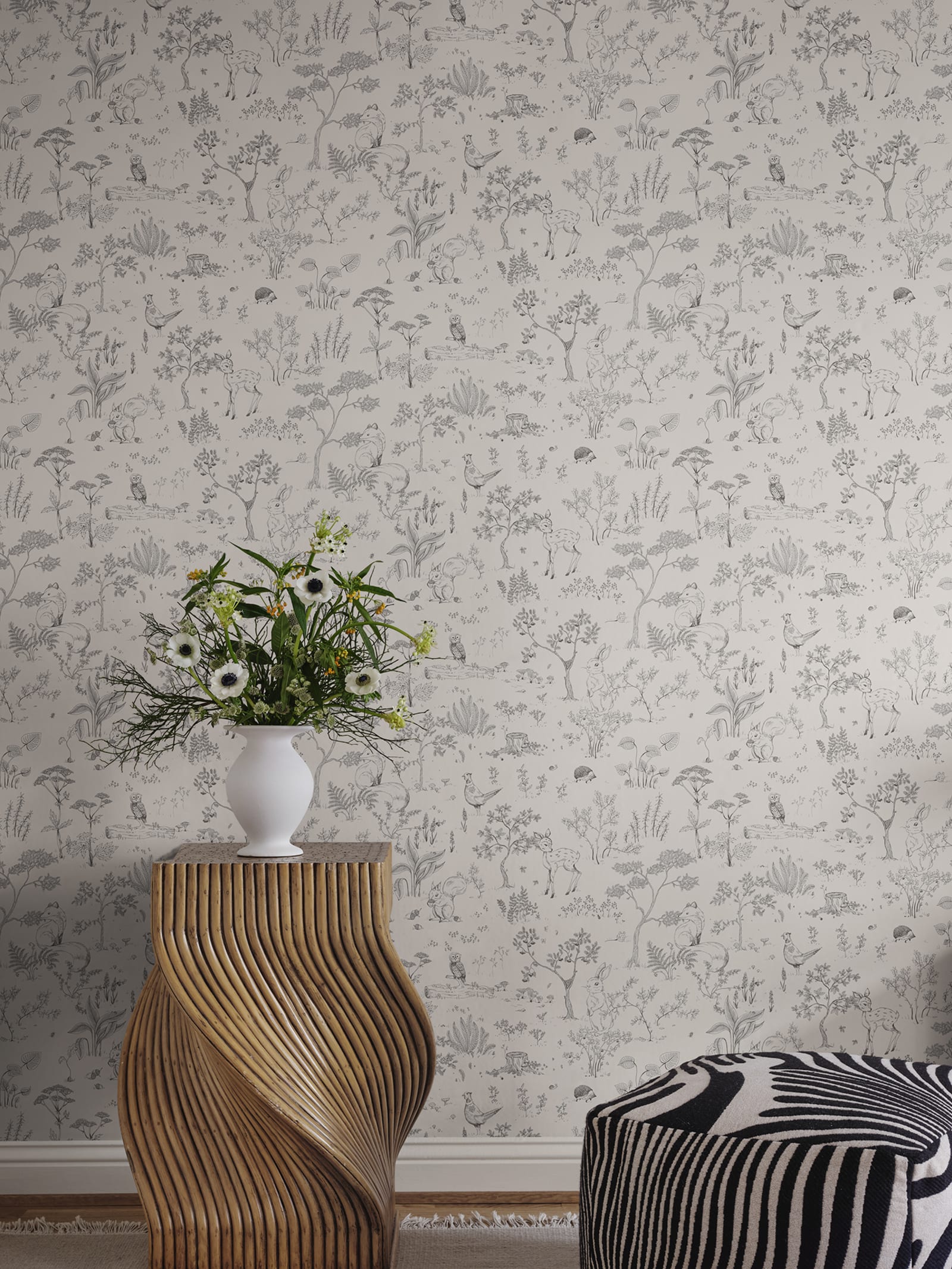 Hollie wallpaper by Sandberg in soft grey woodland print with a sculptural wooden side table and white vase