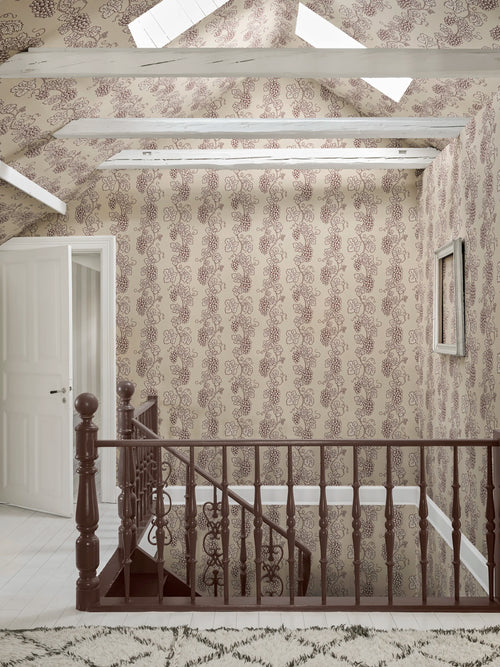 Carla wallpaper by Sandberg on a stairwell landing under sloped beamed ceiling, subtle grapevine pattern in muted red on cream