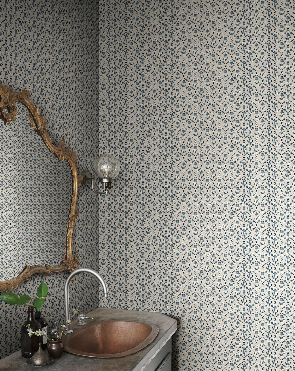 Elena blue floral wallpaper by Sandberg in a powder room, branch-framed mirror above a hammered copper basin and stone vanity
