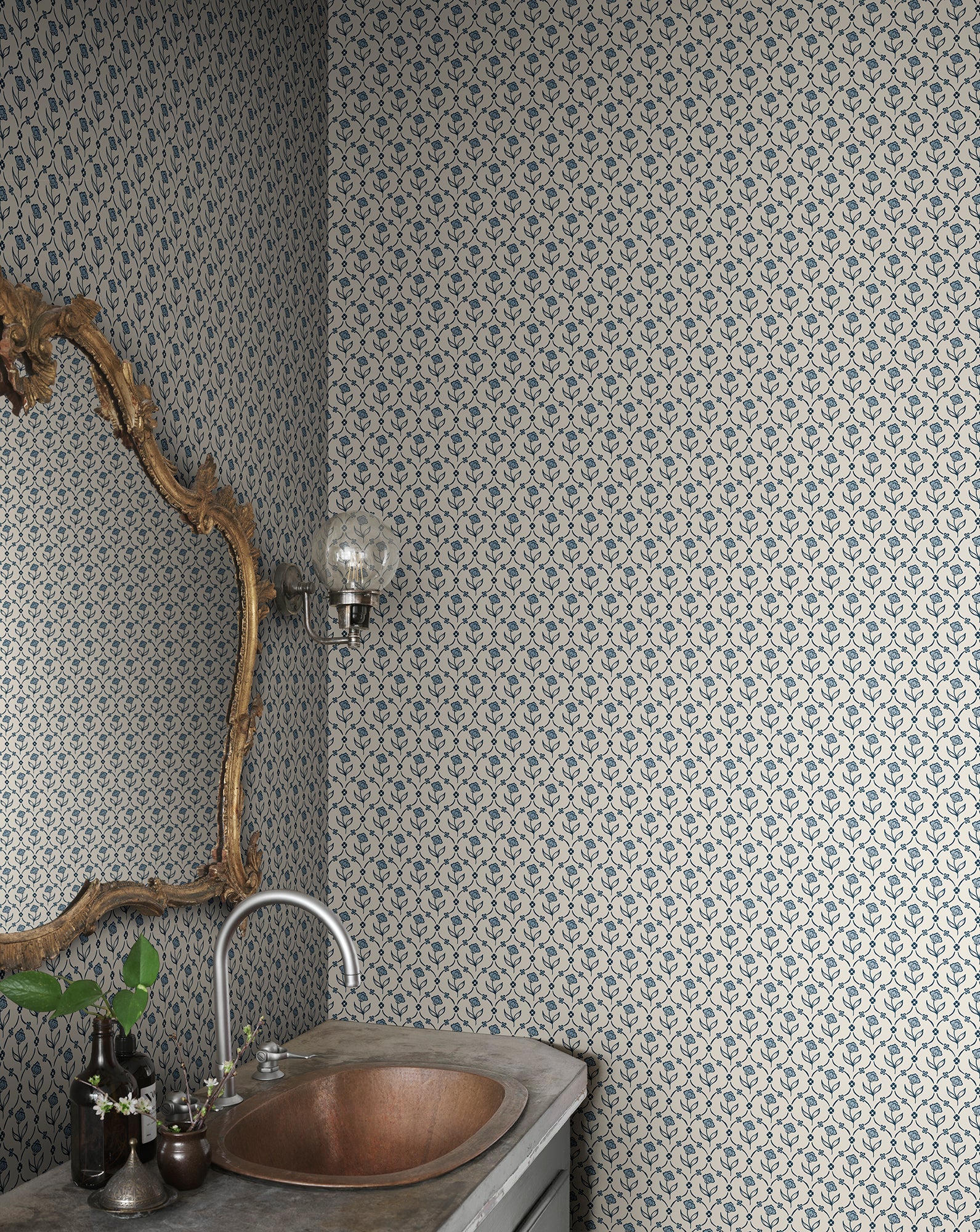 Elena blue floral wallpaper by Sandberg in a powder room, branch-framed mirror above a hammered copper basin and stone vanity