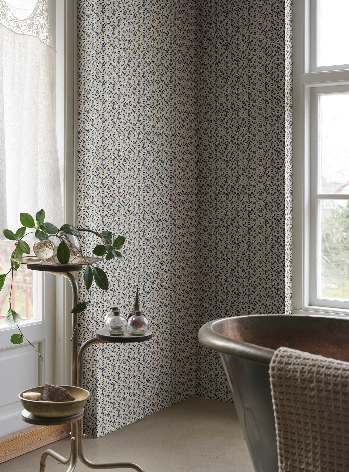 Elena blue floral wallpaper by Sandberg in a bathroom corner, metal copper tub by a window with a trailing plant on a side stand