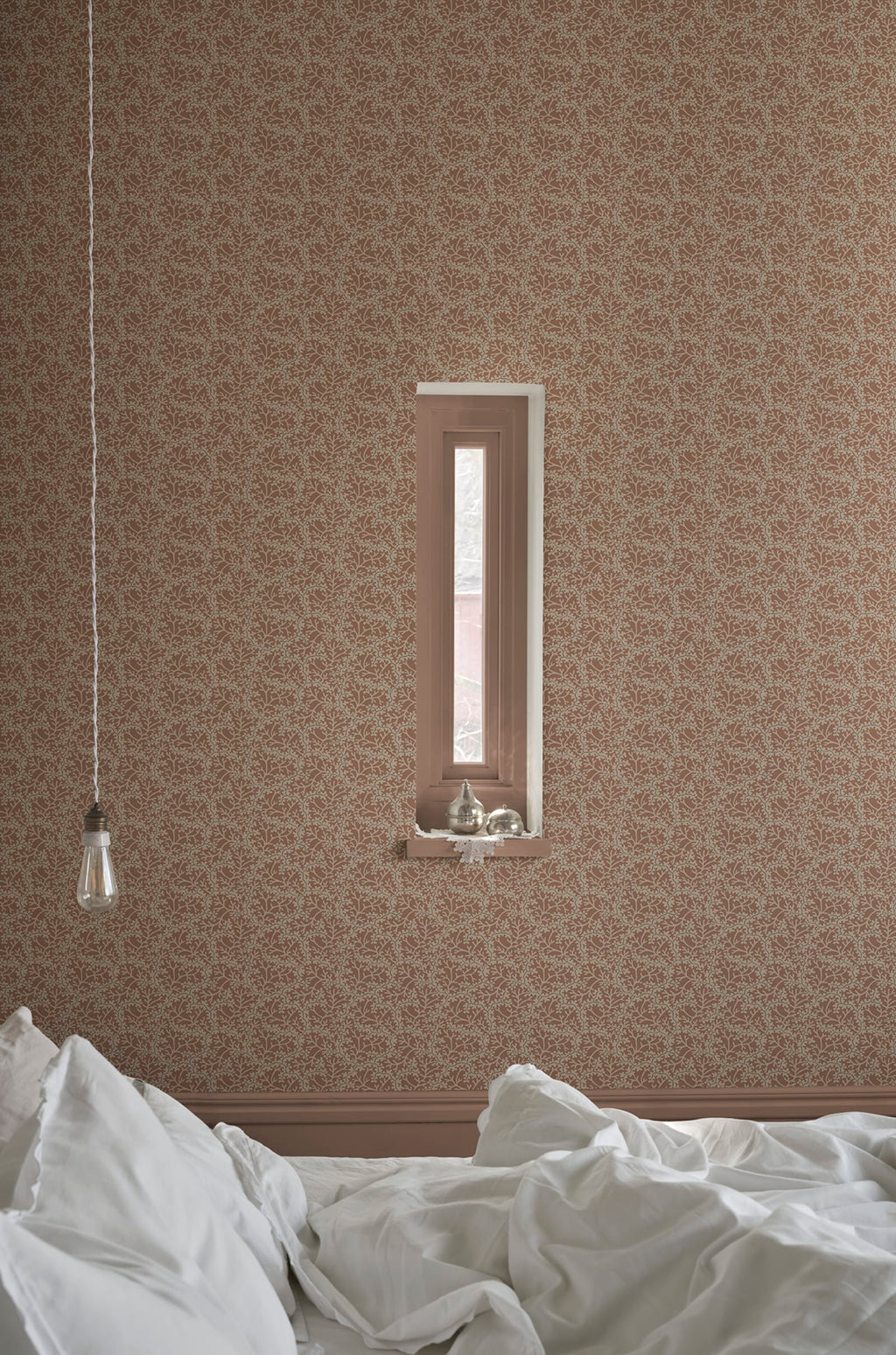 Coral wallpaper by Sandberg in warm clay, styled in a bedroom with a recessed window and rumpled white bedding