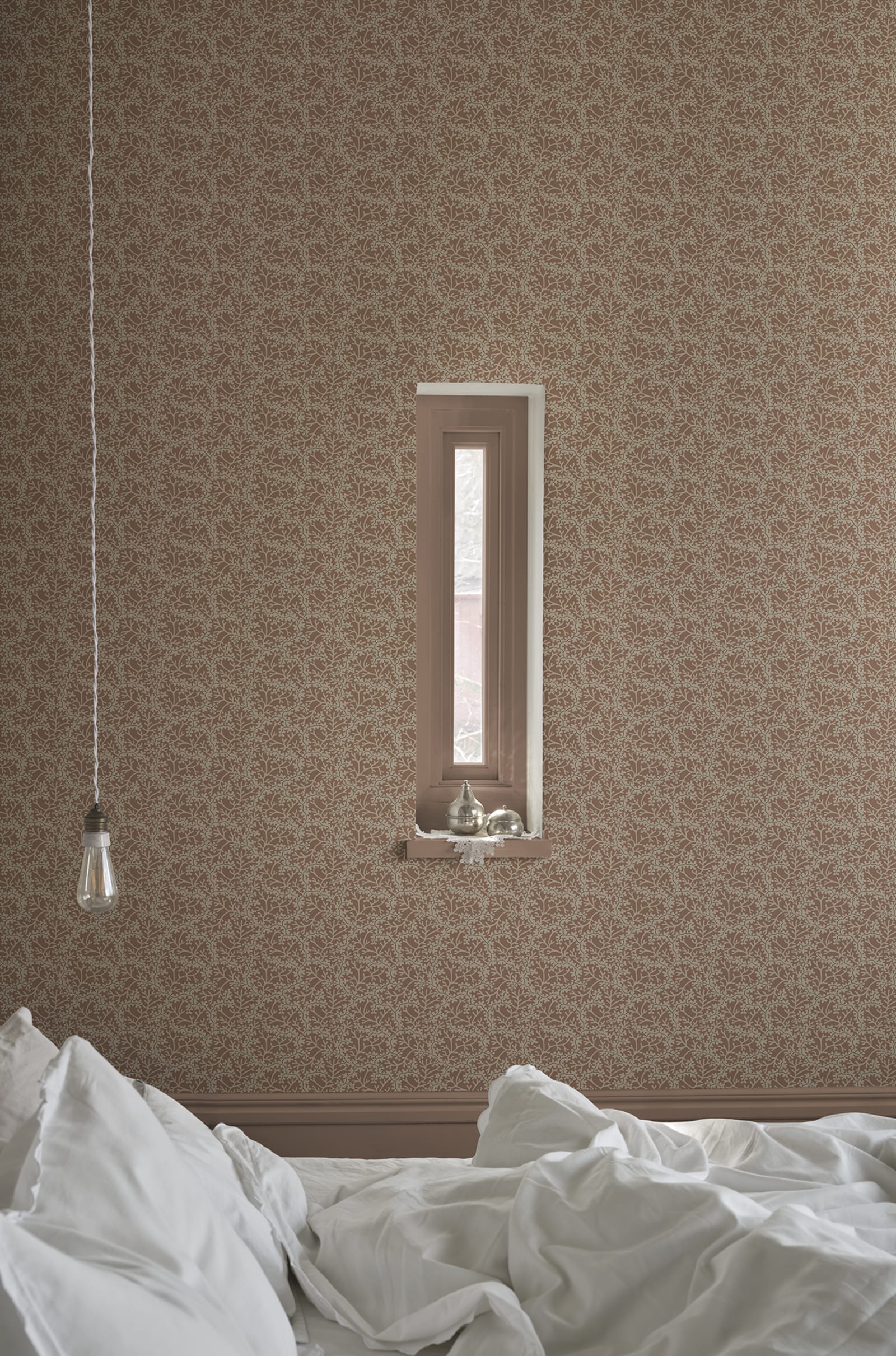Coral wallpaper by Sandberg in warm clay, styled in a bedroom with a recessed window and rumpled white bedding