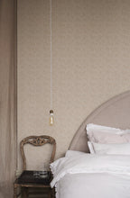 Coral wallpaper by Sandberg in tonal sand, small coral-branch motif styled behind a linen bed with antique chair and pendant bulb